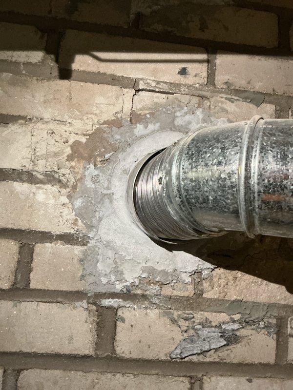 Inspected the water heater, which was leaking at the base and had lost efficiency with age, and confirmed the tank had failed and required replacement. Verified the temperature-and-pressure relief valve and discharge piping were properly routed to the floor drain, and checked the flue vent connection at the masonry wall, noting the deteriorated mortar patch around the vent opening.