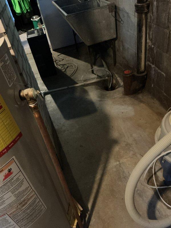 Inspected the water heater, which was leaking at the base and had lost efficiency with age, and confirmed the tank had failed and required replacement. Verified the temperature-and-pressure relief valve and discharge piping were properly routed to the floor drain, and checked the flue vent connection at the masonry wall, noting the deteriorated mortar patch around the vent opening.