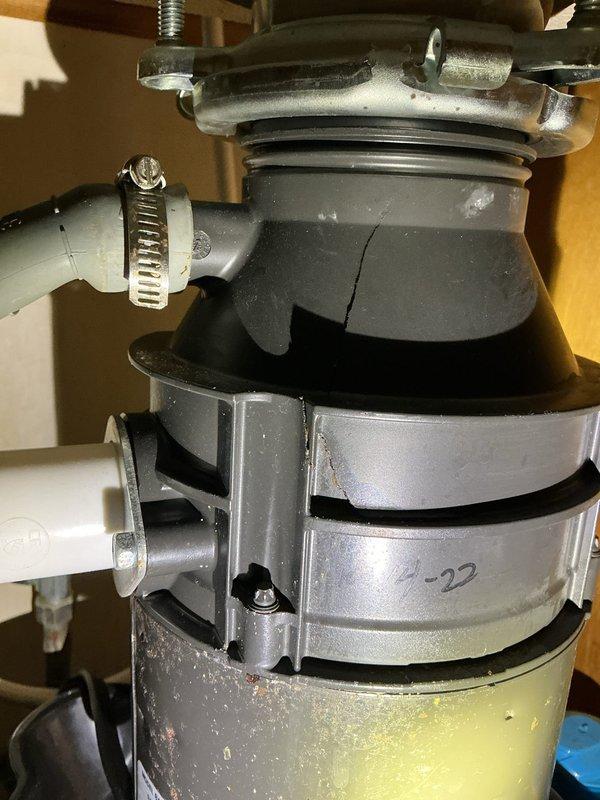 Diagnosed the under-sink leak and traced the source to the garbage disposal unit, which has a cracked rubber splash guard/hopper and a hairline crack in the housing seam, along with significant corrosion and rust staining on the lower canister. The drain hose, clamp, and PVC connection were inspected and ruled out as leak points. The disposal is beyond serviceable repair and replacement is recommended; a bucket was left in place to catch residual water until the unit is replaced.