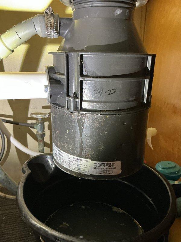 Diagnosed the under-sink leak and traced the source to the garbage disposal unit, which has a cracked rubber splash guard/hopper and a hairline crack in the housing seam, along with significant corrosion and rust staining on the lower canister. The drain hose, clamp, and PVC connection were inspected and ruled out as leak points. The disposal is beyond serviceable repair and replacement is recommended; a bucket was left in place to catch residual water until the unit is replaced.