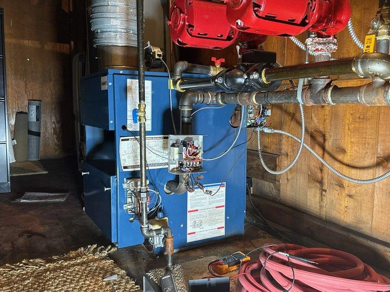 Responded to a no-heat call on a hot water boiler system with two zone circulator pumps and inspected the boiler's control wiring, thermostat terminal connections, and relay/transformer assembly. Dense, tangled wiring and multiple spliced connections were noted in the control box; diagnostic testing was performed with a multimeter to isolate the cause of the loss of heat and verify circuit continuity.
