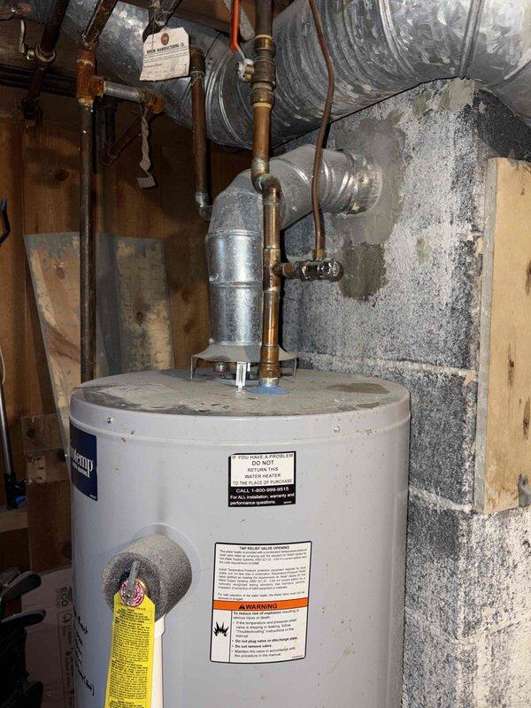 Inspected a 9-year-old gas tank water heater with no hot water due to an extinguished pilot light and a non-functioning relight mechanism. Evaluated the gas control valve assembly, pilot system, and flue connection for the cause of the pilot failure and ignition fault. The unit is installed in a drain pan with a vented flue in the basement utility space and was documented with photos of the tank, labels, and surrounding piping.