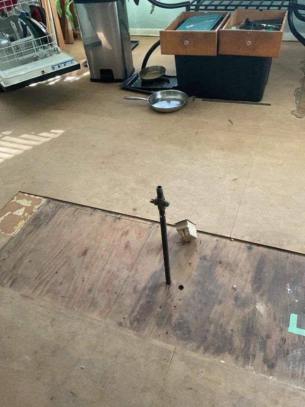 Assessed the abandoned kitchen gas line formerly serving a range, noting an exposed rust-colored steel riser with a brass fitting protruding through the subfloor, and confirmed accessible routing from the basement below. Scope of work to be performed includes shutting off and isolating the gas supply, cutting and removing the abandoned riser, installing a threaded cap on the remaining line, and pressure testing the capped connection for leaks. A 30-minute courtesy call will be made prior to arrival.
