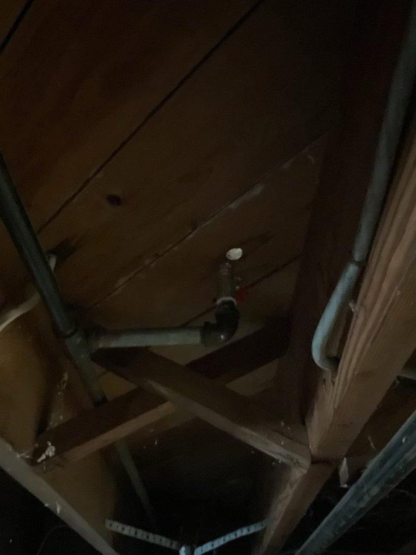 Assessed the abandoned kitchen gas line formerly serving a range, noting an exposed rust-colored steel riser with a brass fitting protruding through the subfloor, and confirmed accessible routing from the basement below. Scope of work to be performed includes shutting off and isolating the gas supply, cutting and removing the abandoned riser, installing a threaded cap on the remaining line, and pressure testing the capped connection for leaks. A 30-minute courtesy call will be made prior to arrival.