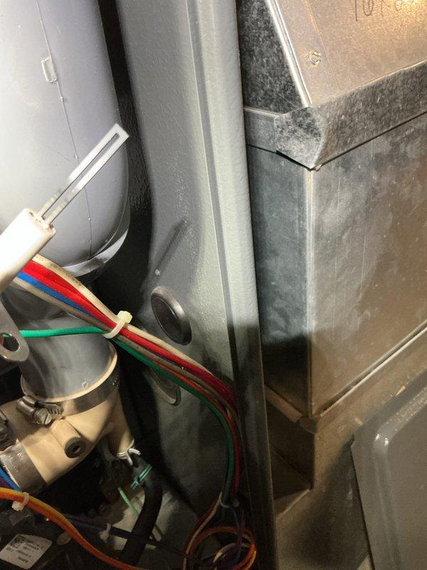Performed a complete furnace super tune-up on an 18-year-old unit, inspecting the blower compartment, inducer/venting assembly, flame sensor, and low-voltage and line-voltage wiring harnesses. Documented rust staining and debris on the cabinet floor near the wire grommet, along with aged, dusty components and loose wiring, and verified ground connection and wire securement. Unit was cleaned and operation verified; recommended monitoring corrosion and aging components due to the furnace's age.