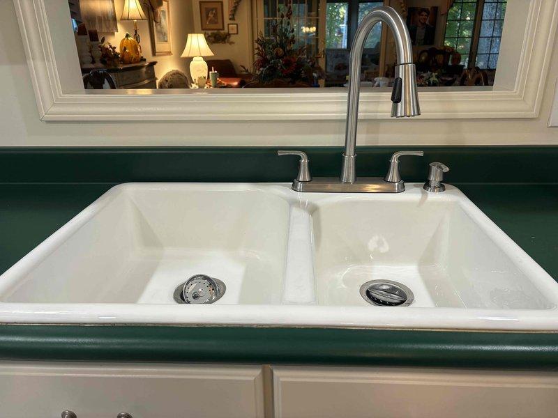 Removed the existing kitchen faucet and garbage disposal from the double-basin sink and installed the customer-supplied brushed stainless pull-down faucet with matching soap dispenser. Reconnected the angle stop valves and supply lines, restored the drain assembly with the dishwasher drain line, and verified proper operation with no leaks.