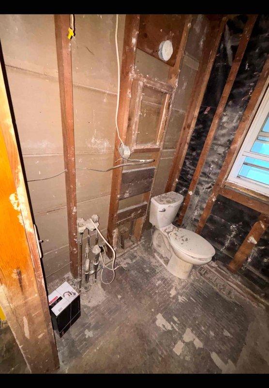 Performed an on-site plumbing estimate for an owner-occupied single-family home undergoing a bathroom remodel, assessing the gutted space with exposed wall framing, existing copper supply stubs with shut-off valves, a floor drain access pocket, and the in-place toilet. Documented existing rough-in conditions and photographed the work area to determine the scope of plumbing modifications and fixture installation required.