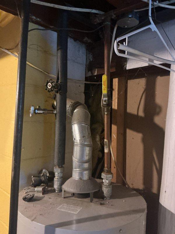 Responded to a follow-up complaint on a 20-year-old atmospheric tank water heater with a burner that would not stay lit following recent furnace replacement. Inspected the unit, including the gas supply and shutoff valve, draft hood, and flue venting connection, to evaluate pilot and burner operation and potential venting or draft issues related to the new furnace installation.
