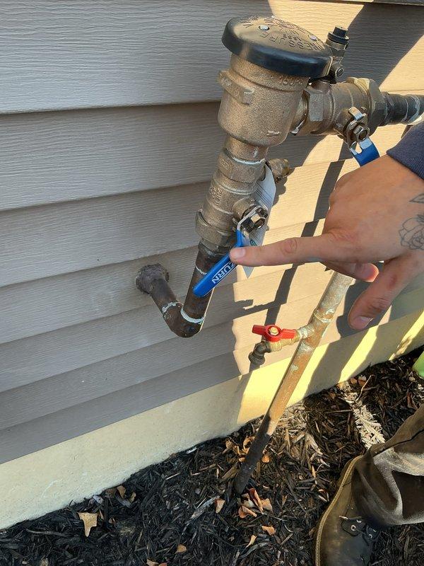 Performed on-site evaluation of an exterior hose bib and backflow preventer assembly to assess relocation of the outside faucet line to facilitate irrigation system drain-down. Inspected the existing brass backflow preventer with dual ball isolation valves, noting a weathered, tarnished supply line alongside newly installed copper piping with a tee fitting and hose-bib outlet. Documented existing conditions with photographs and evaluated routing options to establish scope of work for the proposed relocation.