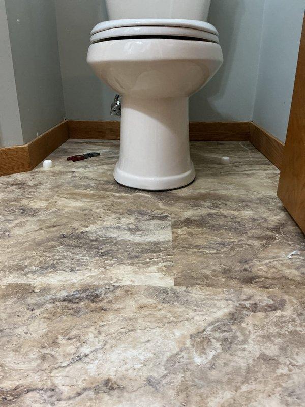 Responded to a follow-up complaint of a leaking toilet and a kitchen faucet sprayer that would not shut off. Pulled the toilet, removed the failed wax seal residue from the drain outlet, and reset the toilet on a new seal over the newly installed vinyl plank flooring. Secured the base and checked the supply line and valve connections for leaks. Kitchen faucet and sprayer replacement was requested but not confirmed in the photos, so warranty review and replacement status should be verified separately.