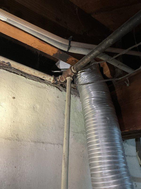 Assessed the basement laundry area to evaluate disconnecting the gas supply line to the dryer and replacing the gas valve connection. Documented existing gas piping, including corrosion at a fitting and flaking paint on adjacent pipe runs, along with the dryer vent routing and surrounding electrical conduit, to scope the work required for the gas line disconnect and valve replacement.