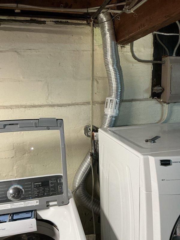 Assessed the basement laundry area to evaluate disconnecting the gas supply line to the dryer and replacing the gas valve connection. Documented existing gas piping, including corrosion at a fitting and flaking paint on adjacent pipe runs, along with the dryer vent routing and surrounding electrical conduit, to scope the work required for the gas line disconnect and valve replacement.