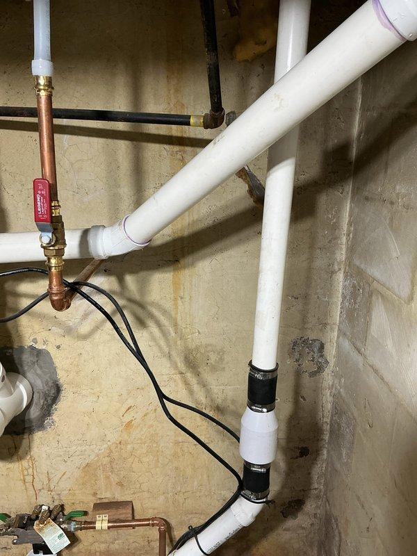 Performed an on-site plumbing evaluation of an unconnected sink drain and documented existing conditions with photographs. Observed PVC DWV piping with a cleanout and rubber couplings near the main drain stack, which is suitable for tying in the sink drain, along with copper supply lines, a ball valve, and wall staining in the adjacent area. Scoped the work to connect the sink drain to the main sewer line and confirmed the project details for proposal.