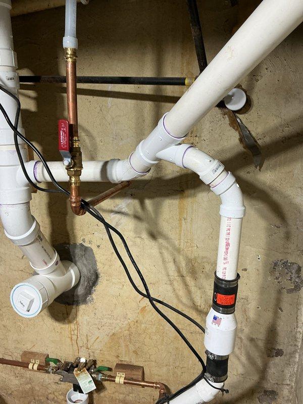 Performed an on-site plumbing evaluation of an unconnected sink drain and documented existing conditions with photographs. Observed PVC DWV piping with a cleanout and rubber couplings near the main drain stack, which is suitable for tying in the sink drain, along with copper supply lines, a ball valve, and wall staining in the adjacent area. Scoped the work to connect the sink drain to the main sewer line and confirmed the project details for proposal.