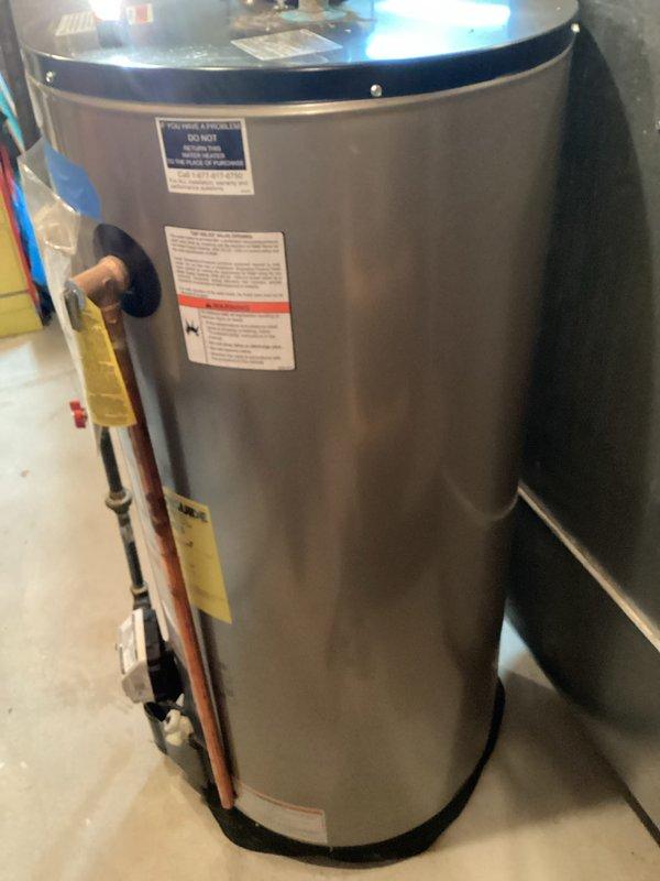 Inspected the gas-fired water heater, including the gas control valve, gas supply line, flue connection, and copper water piping, to prepare a replacement estimate. Noted mineral deposits, discoloration, and moisture around the copper pipe fitting at the top of the tank, indicating leakage or corrosion at the connection. Documented the unit's condition and photographed the data labels and installation area to support the replacement recommendation.