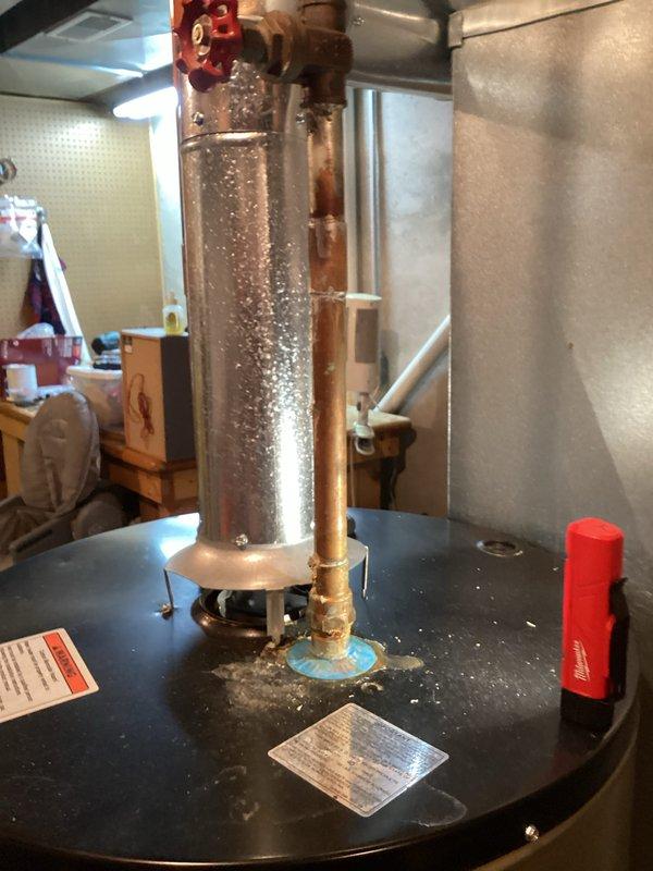 Inspected the gas-fired water heater, including the gas control valve, gas supply line, flue connection, and copper water piping, to prepare a replacement estimate. Noted mineral deposits, discoloration, and moisture around the copper pipe fitting at the top of the tank, indicating leakage or corrosion at the connection. Documented the unit's condition and photographed the data labels and installation area to support the replacement recommendation.