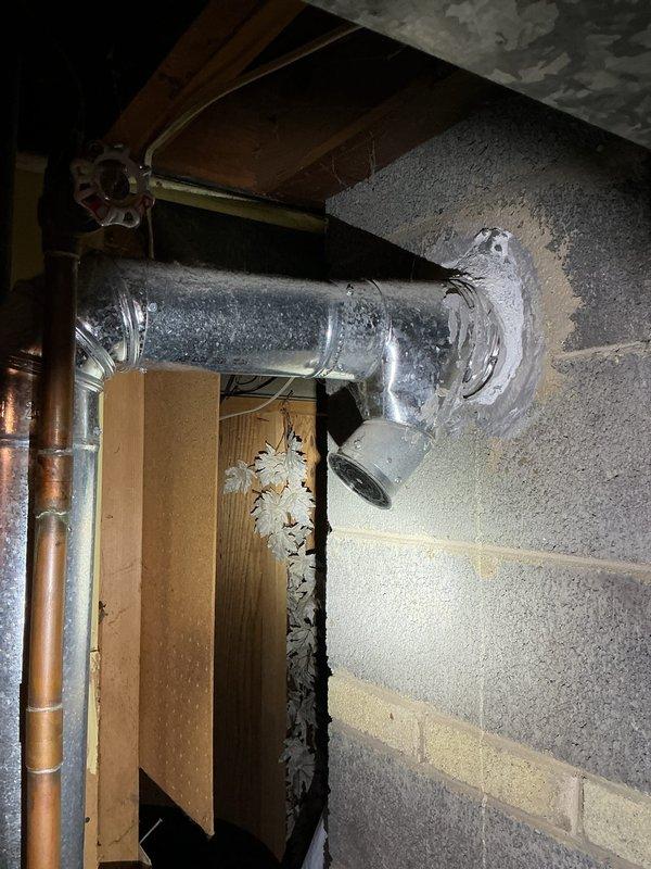 Responded to a reported leak at an 11-year-old tank-style water heater and inspected the unit, associated copper supply piping, shutoff valve, and galvanized flue vent routed through the masonry wall. Documented the condition of the vent penetration, which has a deteriorated cement patch, as well as the items stored on top of the tank, and evaluated the unit for the source of the leak.