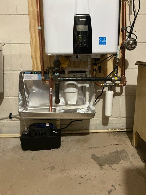 Installed a Navien tankless water heater, wall-mounted on a plywood backer, with new copper supply piping, a brass shut-off valve, black iron gas connections, and a gas shut-off valve. Vented the unit with PVC intake and exhaust piping, and installed a sediment filter on the water line. Routed condensate drainage from the unit through a stainless steel drip pan to a condensate pump to ensure proper discharge.