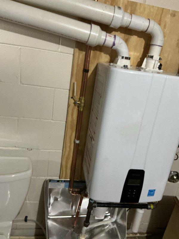 Installed a Navien tankless water heater, wall-mounted on a plywood backer, with new copper supply piping, a brass shut-off valve, black iron gas connections, and a gas shut-off valve. Vented the unit with PVC intake and exhaust piping, and installed a sediment filter on the water line. Routed condensate drainage from the unit through a stainless steel drip pan to a condensate pump to ensure proper discharge.
