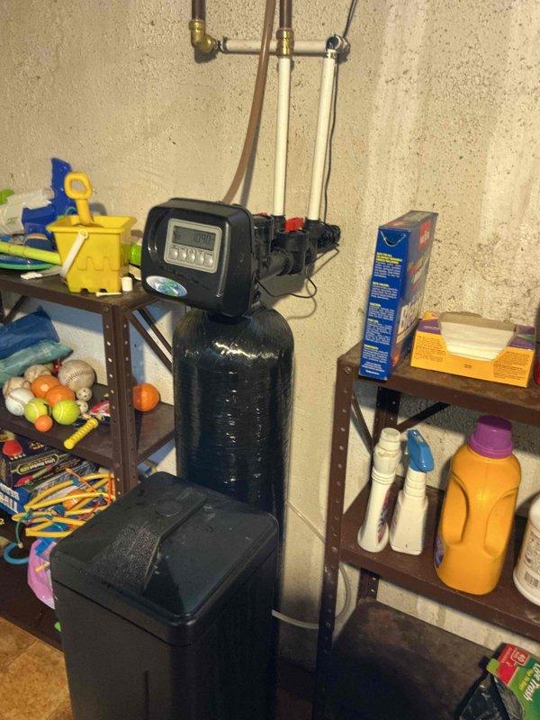 Responded to a water softener leak caused by a component that detached from the bypass valve assembly while the customer attempted to isolate the unit. Inspected the softener, control head, and associated plumbing connections, confirmed the water supply was shut off, and addressed the failed bypass fitting to stop the leak. Documented the unit's condition and surrounding moisture with photos.
