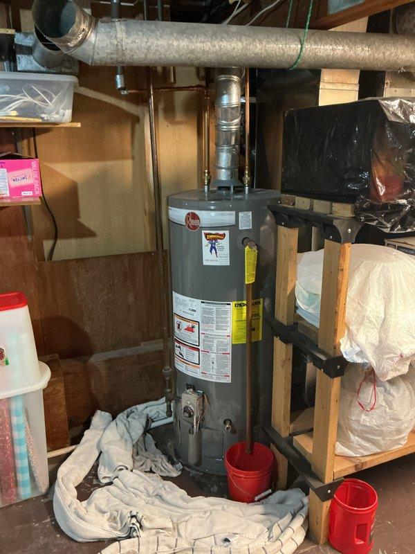 Responded to a reported leak at a gas-fired Rheem water heater and inspected the unit, including the flue connection, supply piping, and base of the tank. Found water pooling at the base with containment buckets and absorbent towels already in place, and no visible corrosion or damage on the top fittings, copper supply lines, or flue assembly. Documented the unit's condition with photos and recommended further evaluation of the tank and relief valve discharge line to pinpoint the leak source and determine whether repair or replacement is required.