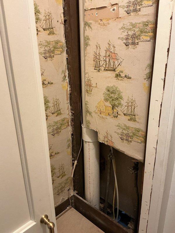 Accessed the wall cavity by removing the cabinet and opening the wallpapered wall section to expose the existing cast iron drain system. Replaced the deteriorated cast iron sections with new white PVC DWV piping, including a wye fitting and branch connection, and joined it to the remaining cast iron using shielded rubber transition couplings secured with stainless steel band clamps. Primed and solvent-welded all PVC joints, supported the vertical stack with pipe clamps, and verified the connections were secure and aligned.