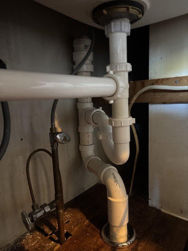 Installed the new sink and reverse osmosis system, connecting the drain assembly with a P-trap and slip-joint fittings and tying into the existing copper supply line with angle-stop valves. Verified all connections were secure and free of leaks, with the under-sink cabinet cleared and the plumbing and electrical supply left properly arranged.