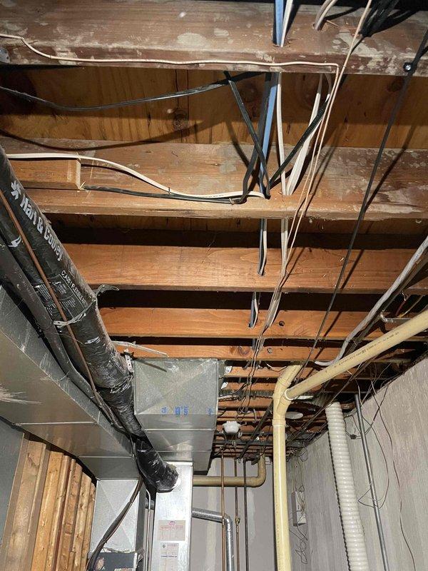 Performed assessment of aging furnace and A/C system in basement for replacement estimate. Current equipment is operational but significantly outdated. Inspection revealed existing ductwork configuration with galvanized metal transitions and exposed utilities, including electrical wiring and plumbing lines running through floor joists, which will need to be considered during replacement planning.