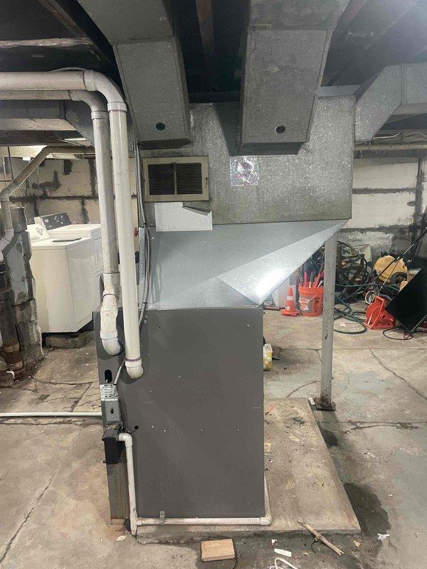 Conducted assessment of 20-year-old furnace and air conditioning system in basement utility area for potential replacement. Documented existing installation, including metal furnace unit with connecting ductwork, drainage system, and surrounding infrastructure. System appears functional but at end of service life; recommended complete HVAC replacement within customer's three-month timeframe.