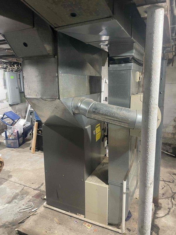 Conducted assessment of 20-year-old furnace and air conditioning system in basement utility area for potential replacement. Documented existing installation, including metal furnace unit with connecting ductwork, drainage system, and surrounding infrastructure. System appears functional but at end of service life; recommended complete HVAC replacement within customer's three-month timeframe.
