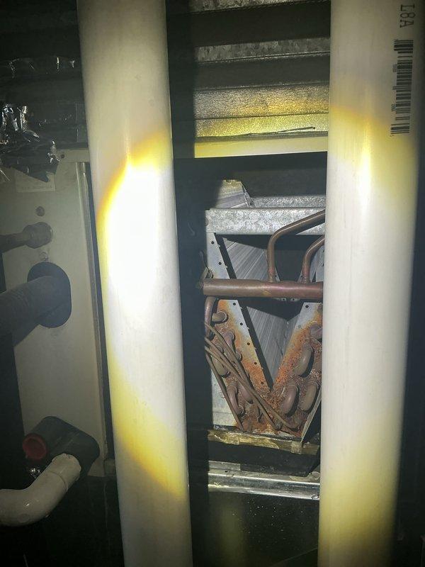 # HVAC Maintenance - ACM Service Summary

Completed annual cooling maintenance service on residential HVAC system. Accessed equipment through confined crawl space storage area and performed comprehensive inspection of cooling components. Documented significant rust and corrosion present on evaporator coil fins, indicating prolonged moisture exposure and age-related deterioration. Photographed corroded heat exchanger elements showing brown and orange oxidation on triangular-shaped metal fins arranged in V-formation within equipment cabinet. Inspected surrounding ductwork, insulation panels, and mechanical enclosure components. System operational at time of service with no immediate performance issues reported. Recommended monitoring equipment performance and consideration of future component replacement due to advanced corrosion on coil assembly.