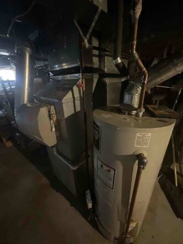 Completed comprehensive estimate for replacement of 14-year-old furnace system located in basement utility room. Inspection included evaluation of existing heating unit, humidifier, thermostat, and hot water tank to determine replacement specifications and system compatibility. Documented current equipment configuration including ductwork connections, venting assembly through exterior wall via PVC piping, and overall mechanical room layout to prepare accurate replacement proposal for residential heating system.