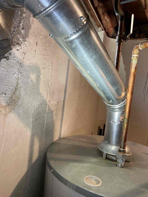 Responded to service call for water intrusion through water heater vent during heavy rainfall. Upon inspection, identified improper vent termination allowing rainwater to enter the flue system and drip from the atmospheric vent hood. Examined the galvanized vent pipe configuration and confirmed lack of adequate weather protection at the exterior termination point. Recommended installation of a proper vent cap or rain collar to prevent future water infiltration while maintaining proper draft and combustion air requirements for the natural draft gas water heater.