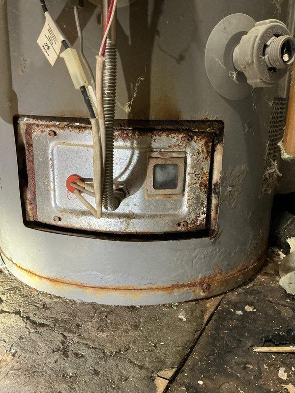 Responded to no hot water call and performed diagnostic inspection of residential water heater. Upon arrival, conducted visual assessment of unit and identified extensive corrosion on lower burner access panel and control assembly area. Documented heavily rusted combustion chamber access panel with significant deterioration around gas control components and pilot assembly viewing port. Water heater showed advanced age with rust streaking on tank exterior and mineral deposits on floor indicating previous moisture exposure. No repairs performed during this visit as unit requires replacement due to extensive corrosion compromising safety and functionality of gas controls and combustion components.