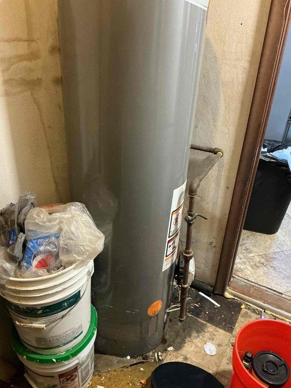 Responded to no hot water call and performed diagnostic inspection of residential water heater. Upon arrival, conducted visual assessment of unit and identified extensive corrosion on lower burner access panel and control assembly area. Documented heavily rusted combustion chamber access panel with significant deterioration around gas control components and pilot assembly viewing port. Water heater showed advanced age with rust streaking on tank exterior and mineral deposits on floor indicating previous moisture exposure. No repairs performed during this visit as unit requires replacement due to extensive corrosion compromising safety and functionality of gas controls and combustion components.