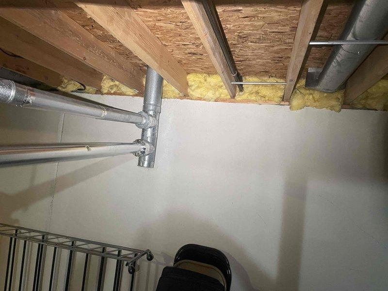 Conducted on-site evaluation of existing HVAC system located in unfinished basement utility area to provide replacement estimate for furnace and air conditioning equipment. Documented current installation consisting of gray vertical air handler/furnace unit with aluminum supply ductwork, flexible white ribbed ducting distribution, and associated copper refrigerant lines with insulation wrapping. Assessed mechanical room layout, existing duct configuration with exposed ceiling joists and fiberglass insulation, clearances, and utility connections to determine equipment replacement requirements and specifications for new system installation.