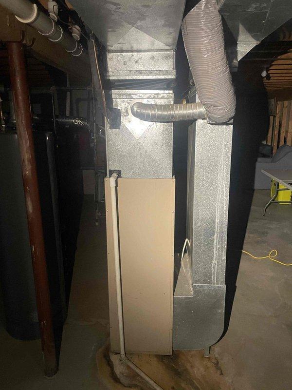 Conducted on-site evaluation of existing HVAC system located in unfinished basement utility area to provide replacement estimate for furnace and air conditioning equipment. Documented current installation consisting of gray vertical air handler/furnace unit with aluminum supply ductwork, flexible white ribbed ducting distribution, and associated copper refrigerant lines with insulation wrapping. Assessed mechanical room layout, existing duct configuration with exposed ceiling joists and fiberglass insulation, clearances, and utility connections to determine equipment replacement requirements and specifications for new system installation.