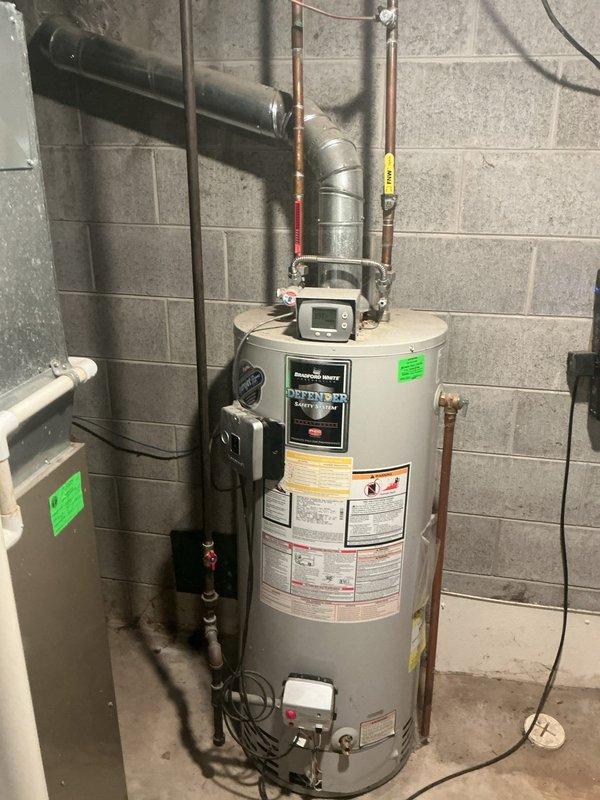 # Tanked Water Heater Service

Responded to service call for a 14-year-old Bradford White tanked water heater located in basement utility area. Performed diagnostic inspection of unit including evaluation of all plumbing connections, pressure relief valve, discharge piping, and copper supply lines. Documented existing conditions with photography showing water heater installation, piping configuration with color-coded tape markings, and digital control unit mounted on top of tank.

Inspected galvanized vent pipe penetration through concrete block wall, noting significant white mineral deposits and crystalline buildup around wall penetration point, indicating potential moisture or condensation issues requiring monitoring. Evaluated all visible plumbing infrastructure, electrical connections, and mechanical components for proper operation and code compliance.

No warranty coverage applicable for parts or labor on this service visit.
