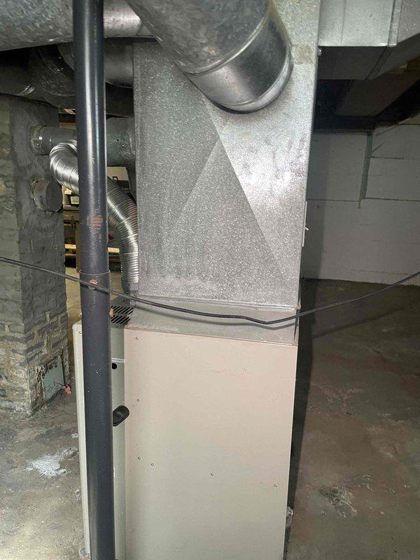 Conducted comprehensive site evaluation for full HVAC system replacement in residential property currently lacking air conditioning. Assessed existing 15-year-old Gibson furnace installation in basement utility area, documenting current heating infrastructure including extensive flexible aluminum ductwork network with multiple branches and elbows throughout ceiling space. Evaluated existing duct connections, metal clamps, and tape sealing at junction points. Photographed furnace unit with two-tone gray and beige cabinet configuration, cylindrical supply plenum, and associated gas line and electrical connections. Inspected concrete block foundation walls, basement layout constraints, and available space for new equipment installation. Provided detailed estimate for complete HVAC system installation including new central air conditioning unit to meet customer's timeline of replacement within the next couple weeks.