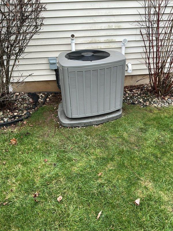 Completed routine annual maintenance on residential air conditioning system. Performed comprehensive tune-up on 1-year-old AC unit located on exterior concrete pad. Inspected condenser unit housing, verified proper clearance from structure, and confirmed secure mounting on level pad. Checked refrigerant lines and PVC condensate drainage system for proper installation and function. Cleaned condenser coils and removed debris from unit exterior and surrounding area. Inspected fan motor, blades, and protective grille for proper operation and structural integrity. Verified electrical connections and conduit are secure. Tested system startup and operational parameters. Unit found in good working condition with no issues identified. All components functioning within manufacturer specifications. System ready for cooling season operation.