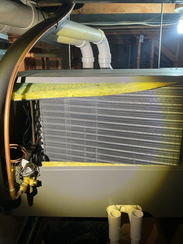 # HVAC Maintenance - ACM Service Completed

Performed comprehensive Air Care Cooling maintenance on residential HVAC system located in basement mechanical room. Conducted thorough inspection of air handling unit mounted on elevated green support rails with associated ductwork and piping systems.

## Equipment Inspection and Findings

Inspected primary air handling unit and evaporator coil assembly. Visual examination revealed significant biological growth present on evaporator coil surfaces, evidenced by yellow-green substance covering portions of the aluminum fin array, particularly concentrated along top edges and distributed across multiple sections of the coil. This growth pattern indicates moisture accumulation and potential drainage concerns that can reduce system efficiency and indoor air quality.

Verified all refrigerant line connections, including copper lines with brass fittings and associated black insulation material. Examined PVC condensate drainage piping with curved elb