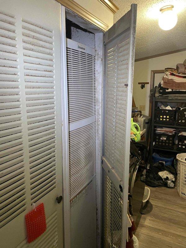 Provided estimate for replacement of non-operational air conditioning system at single-story ranch home. Current outdoor condensing unit dating from 1990s located beneath deck shows significant age-related deterioration and debris accumulation. Indoor air handler/furnace from 2017 housed in main level utility closet with louvered door access remains functional. Estimate covers A/C system replacement only, maintaining existing natural gas furnace equipment.