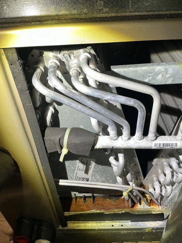 # HVAC Maintenance Service Completed

Performed scheduled air conditioning maintenance on residential HVAC system. Upon inspection, discovered severely frosted evaporator coils indicating restricted airflow or potential refrigerant issues. The frost accumulation was extensive across all serpentine coil tubes and header manifold, requiring immediate attention. Noted corrosion present in drain pan beneath coils, suggesting ongoing moisture management concerns.

Replaced air filter and evaporator pad as part of routine maintenance protocol. Inspected air handler unit and associated ductwork connections. All manufacturer labels and safety warnings verified as intact and legible. Condensate drain system checked for proper operation. Documented system condition through photographic evidence for maintenance records.

System requires monitoring for proper defrost cycling and airflow restoration following filter replacement.