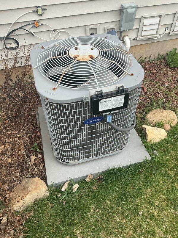 Completed comprehensive AC tune-up on 15-year-old Carrier outdoor condensing unit. Performed standard maintenance protocol including inspection of refrigerant lines, electrical connections, and conduit routing; verified proper operation of compressor and condenser fan motor; cleaned condenser coil and checked airflow through mesh grille. Unit operational and functioning within normal parameters despite visible exterior weathering and rust staining on fan grille assembly, which is cosmetic and does not affect performance at this time.