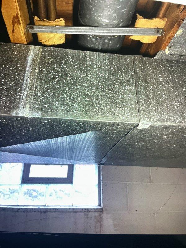 Responded to report of water leaking from ductwork connected to 3-year-old furnace system in basement. Upon inspection, identified moisture infiltration at duct junction near copper plumbing line, with visible water staining on adjacent wooden structural members. Documented conditions showing discoloration patterns on floor joists indicating ongoing moisture exposure. Examined main supply plenum and ductwork connections for condensation issues or external water sources. Photographed affected areas including duct-to-plenum connections and proximity to plumbing penetrations for warranty documentation purposes.