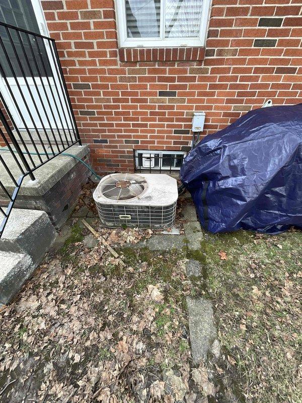 Conducted comprehensive site evaluation for complete HVAC system replacement on residential property with 16-year-old air conditioning system. Assessed existing exterior condenser unit positioned on concrete pad against brick exterior wall, noting beige/tan unit with protective metal grille and mounted electrical disconnect. Evaluated interior equipment including vertical air handler/furnace unit and water heater in basement utility area, documenting ductwork configuration, clearances, and mechanical connections. Photographed both exterior and interior installations to document current system layout, equipment condition, and spatial requirements for proposed full system replacement scheduled within the next couple of weeks.