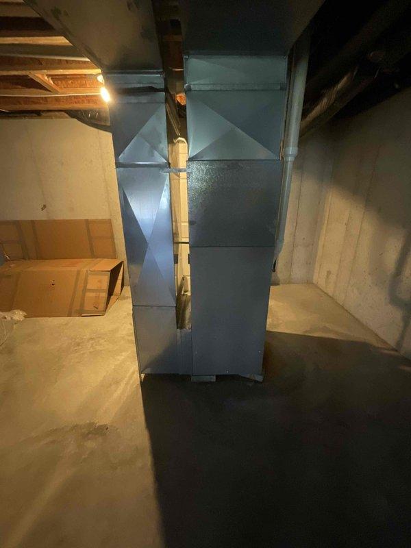 Provided estimate for furnace replacement in basement location. Existing unit is non-operational and has reached end of service life at 20-25 years old. Assessed current HVAC system with light blue painted ductwork extending vertically through exposed ceiling joists. Documented installation area including concrete block walls, concrete flooring, and existing copper piping infrastructure to determine proper equipment sizing and installation requirements for replacement system.