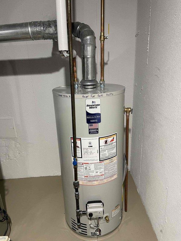 Completed installation of a 40-gallon Bradford White tanked water heater in residential basement utility room. Connected all supply and discharge plumbing lines using copper piping with galvanized fittings, installed gas control valve and connections at base of unit, and secured proper venting with metallic duct work penetrating exterior wall with appropriate sealing. Instructed customer on proper water heater lighting procedures, noting water service would remain off during installation period pending permit approval and final inspection.