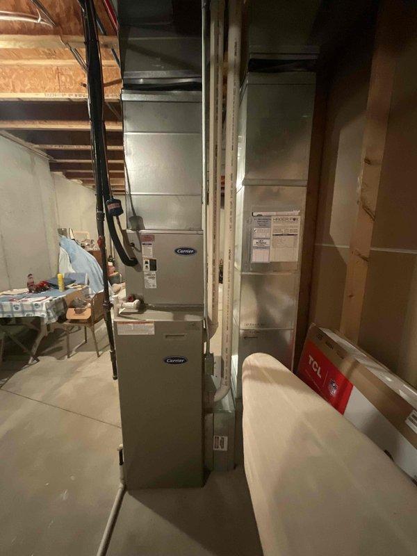 Responded to service call for furnace not maintaining set temperature. Inspected 17+ year old Carrier HVAC system located in basement consisting of stacked air handler and furnace unit. Performed diagnostic evaluation of heating system operation, thermostat communication, and temperature control functionality. Documented equipment condition with photos showing complete system installation including ductwork, electrical connections, and surrounding utility area. Previous service visit conducted nine months prior with service credit applied to current diagnostic assessment.