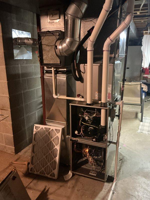 Completed comprehensive annual heating and cooling maintenance on a 10-year-old residential furnace system located in basement installation. Performed full system inspection with access panels removed to evaluate all internal mechanical and electrical components including blower motor assembly, control board, burner compartment, heat exchanger, and gas valve operation. Verified proper pilot light ignition and flame characteristics. Inspected all electrical connections and wiring harnesses for signs of wear or deterioration. Examined ductwork connections and flexible duct transitions at unit plenum. Evaluated air filter condition and verified proper airflow through system. Documented system operation with photographic evidence showing internal components and overall installation condition. All components found operating within normal parameters with no immediate service needs identified.